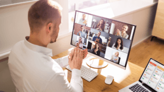 A man applauds along with colleagues in a virtual meeting on a computer monitor